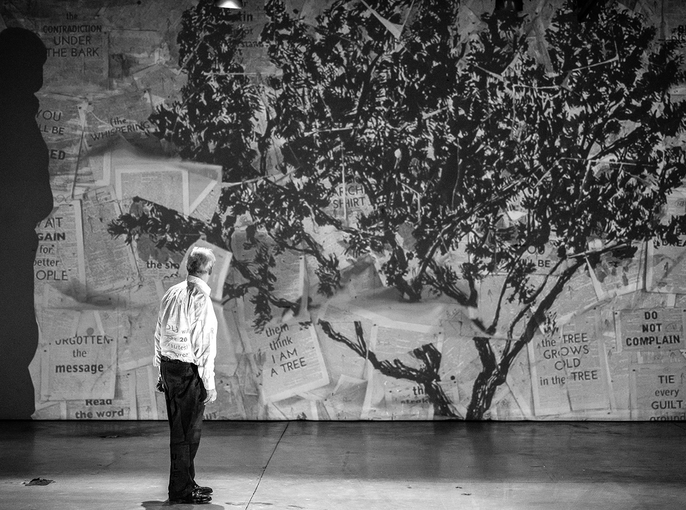 Kentridge sur scène avec son oeuvre projeté sur un mur représentant un arbre.