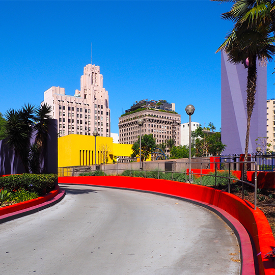 Marius Luscher, photographie d'une route entouré de murs rouges et de bâtiments violets et jaunes, sous un ciel bleu.