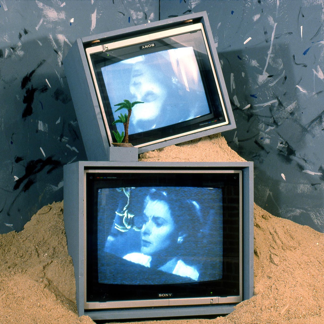 Deux écrans de TV mise l'une sur l'autre posé dans du sable.