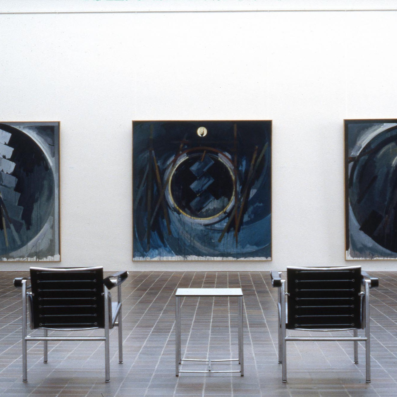 Salle d'exposition présentant trois tableaux sur le mur.