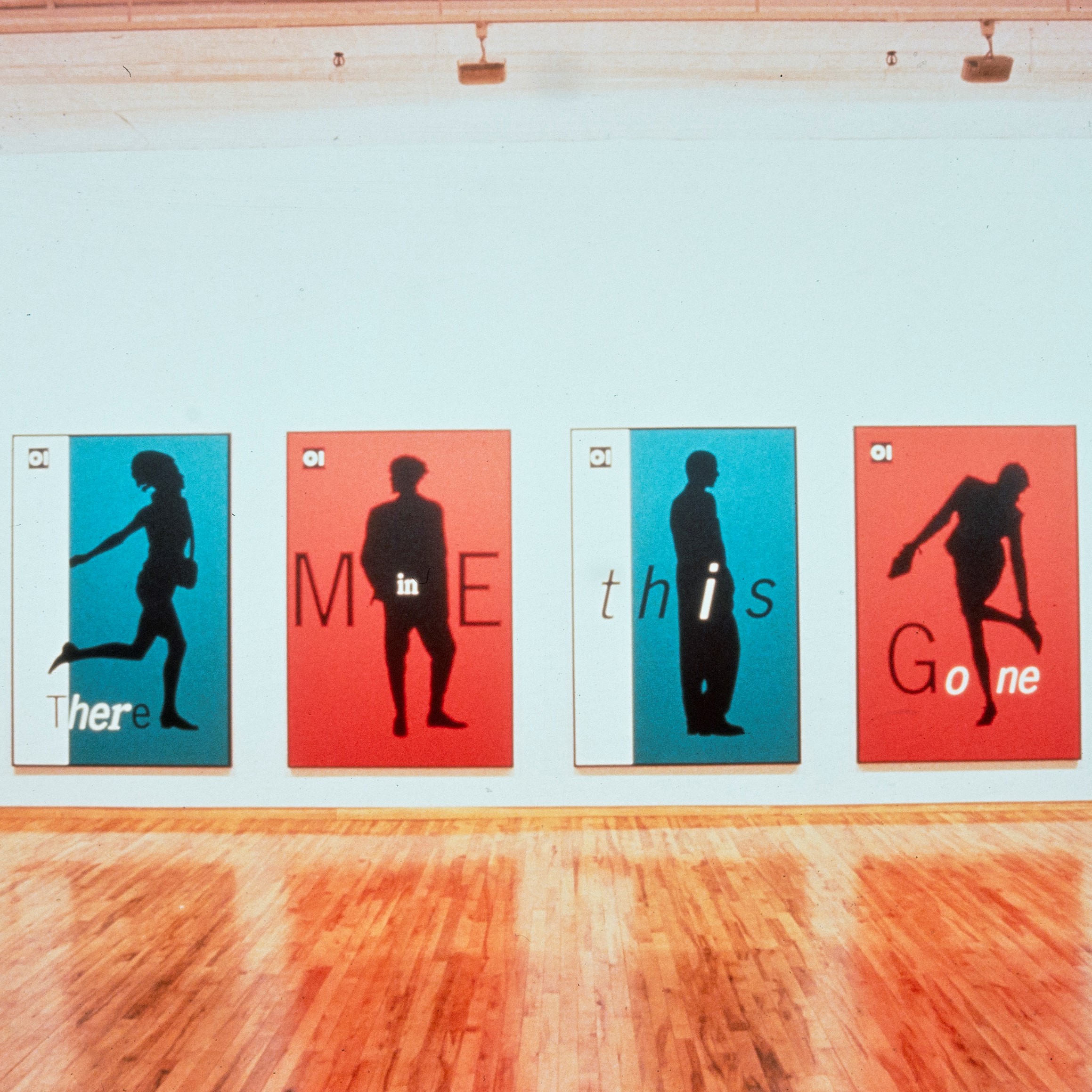 Quatre affiches de couleur bleu ou rouge, accrochées sur un mur blanc du musée.