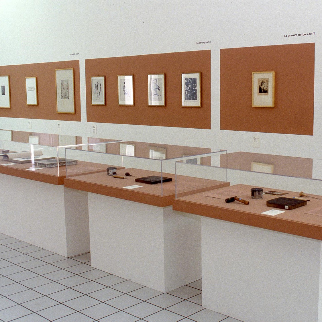 Salle d'exposition avec vitrines et œuvres au mur.