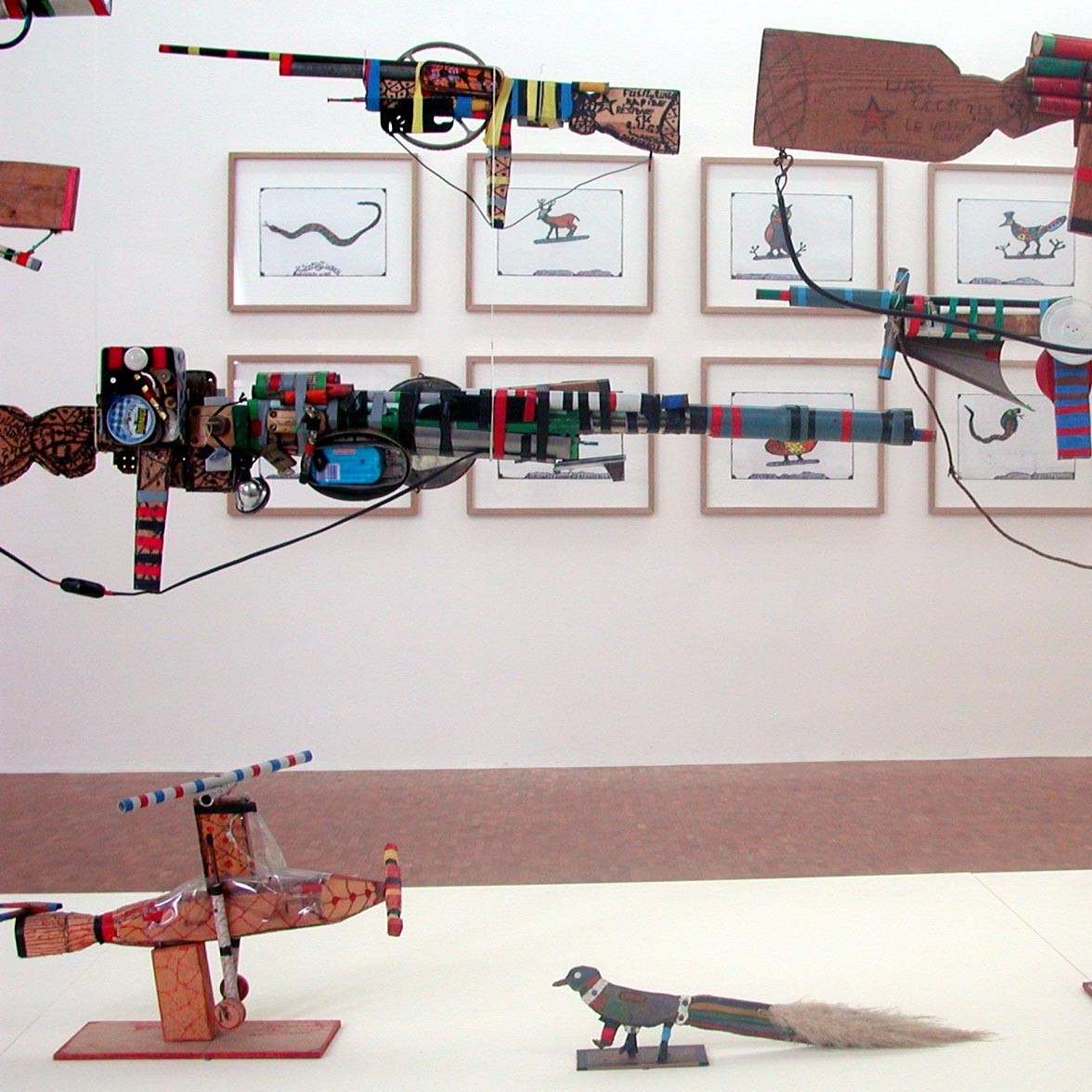 Œuvres représentant des armes en plastique de Robillard suspendues devant des dessins.