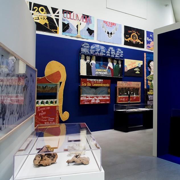 Accrochage salle d'exposition avec vitrines, projections et œuvres.