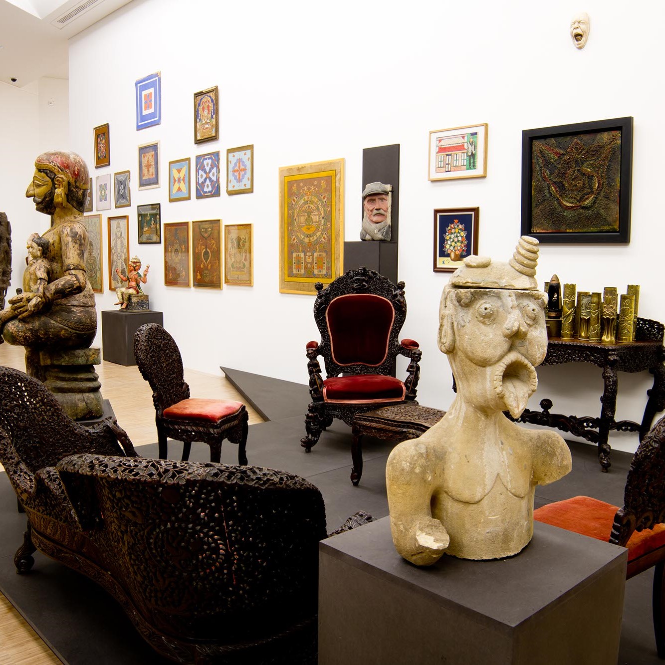 Salle d'exposition avec mobilier, sculptures et toiles au mur.