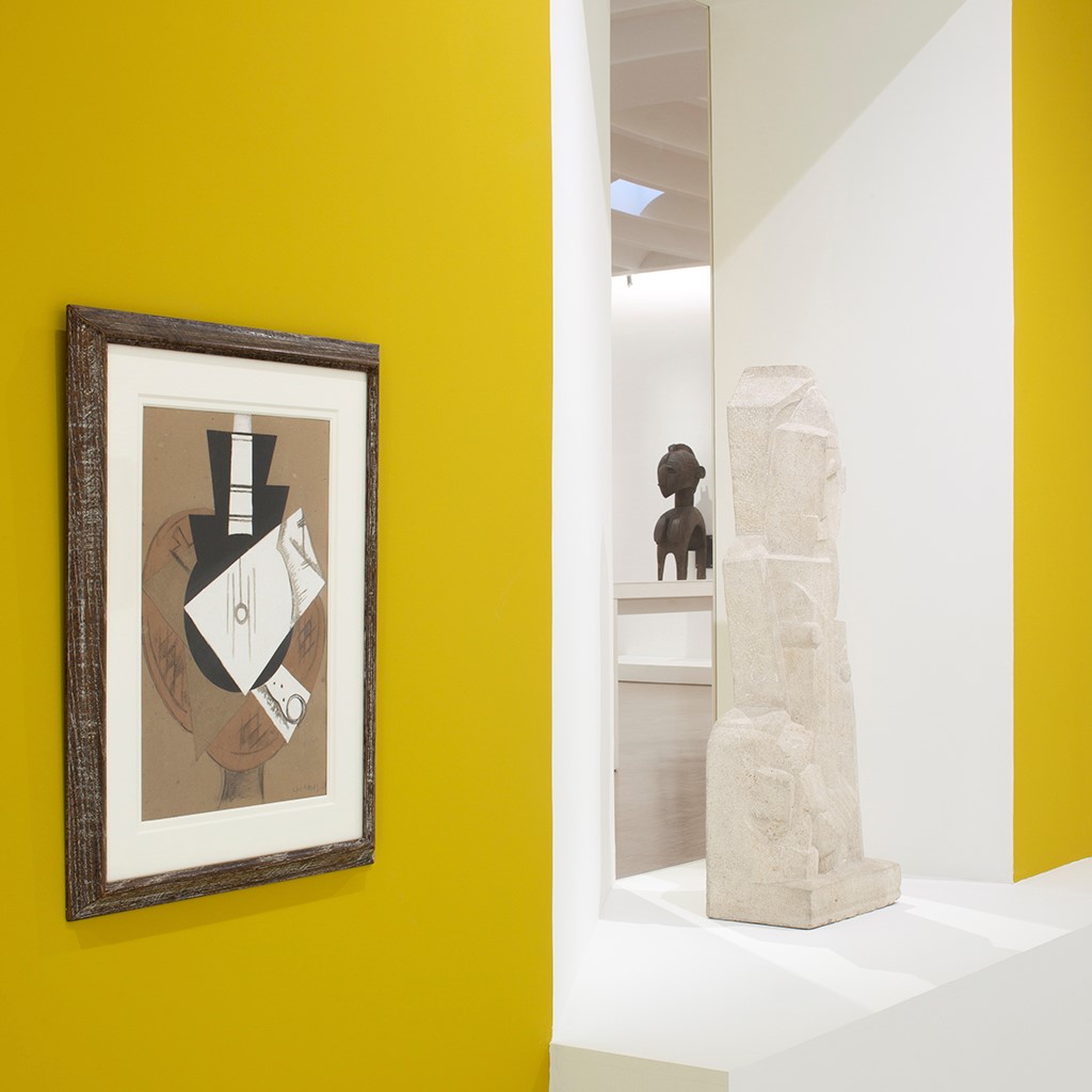 Salle d'exposition jaune et blanche avec toiles et sculptures.