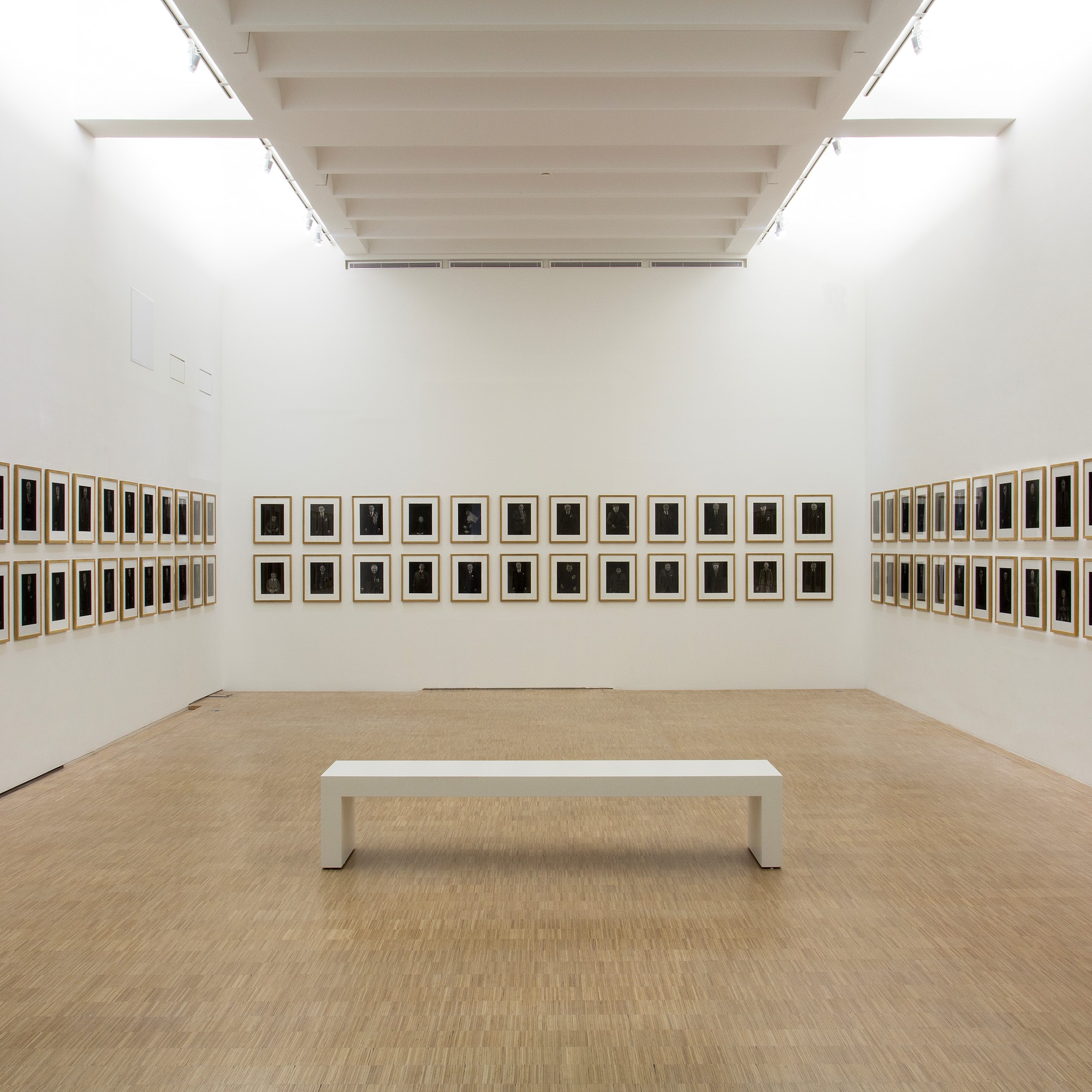 Salle d'exposition avec deux rangés de cadres et un banc.