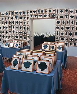 Accumulation de tableaux sur tables et murs d'une salle d'exposition.