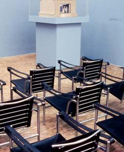 Salle de projection avec chaises tournées vers une petite télé et vitrine.