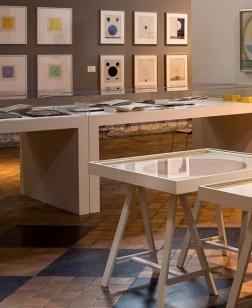 Salle d'exposition avec cimaises, tables et œuvres.