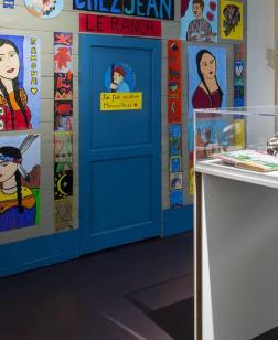 Salle d'exposition avec vitrine en son centre et œuvres aux murs.