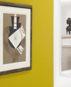 Salle d'exposition jaune et blanche avec toiles et sculptures.