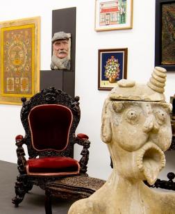Salle d'exposition avec mobilier, sculptures et toiles au mur.