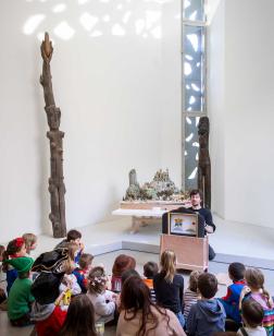 Groupe d'enfants au sol devant un guide qui montre une œuvre, à l'occasion d'un atelier vacances d'été.