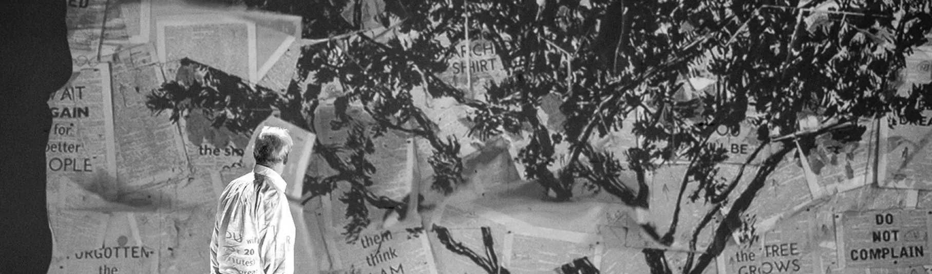 Kentridge sur scène avec son oeuvre projeté sur un mur représentant un arbre.