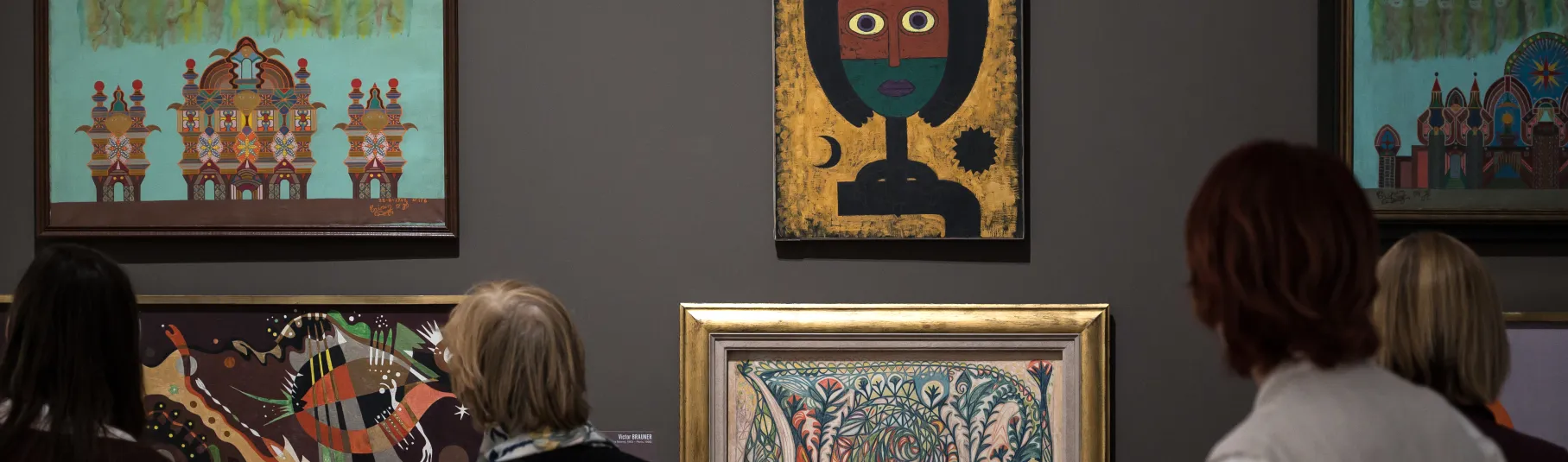 Visiteurs dans une salle d'exposition devant six toiles sur un fond gris. 