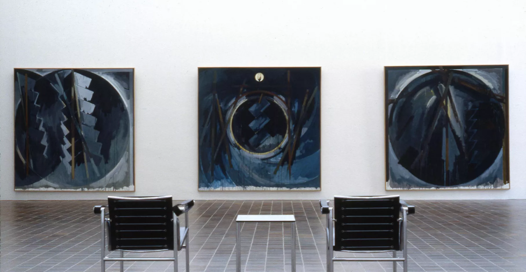 Salle d'exposition présentant trois tableaux sur le mur.