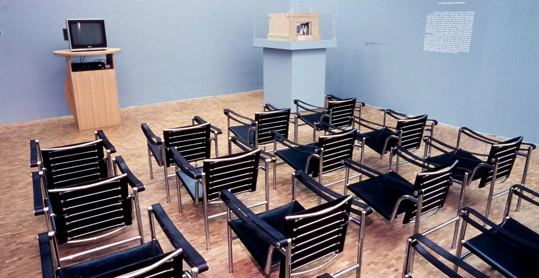 Salle de projection avec chaises tournées vers une petite télé et vitrine.