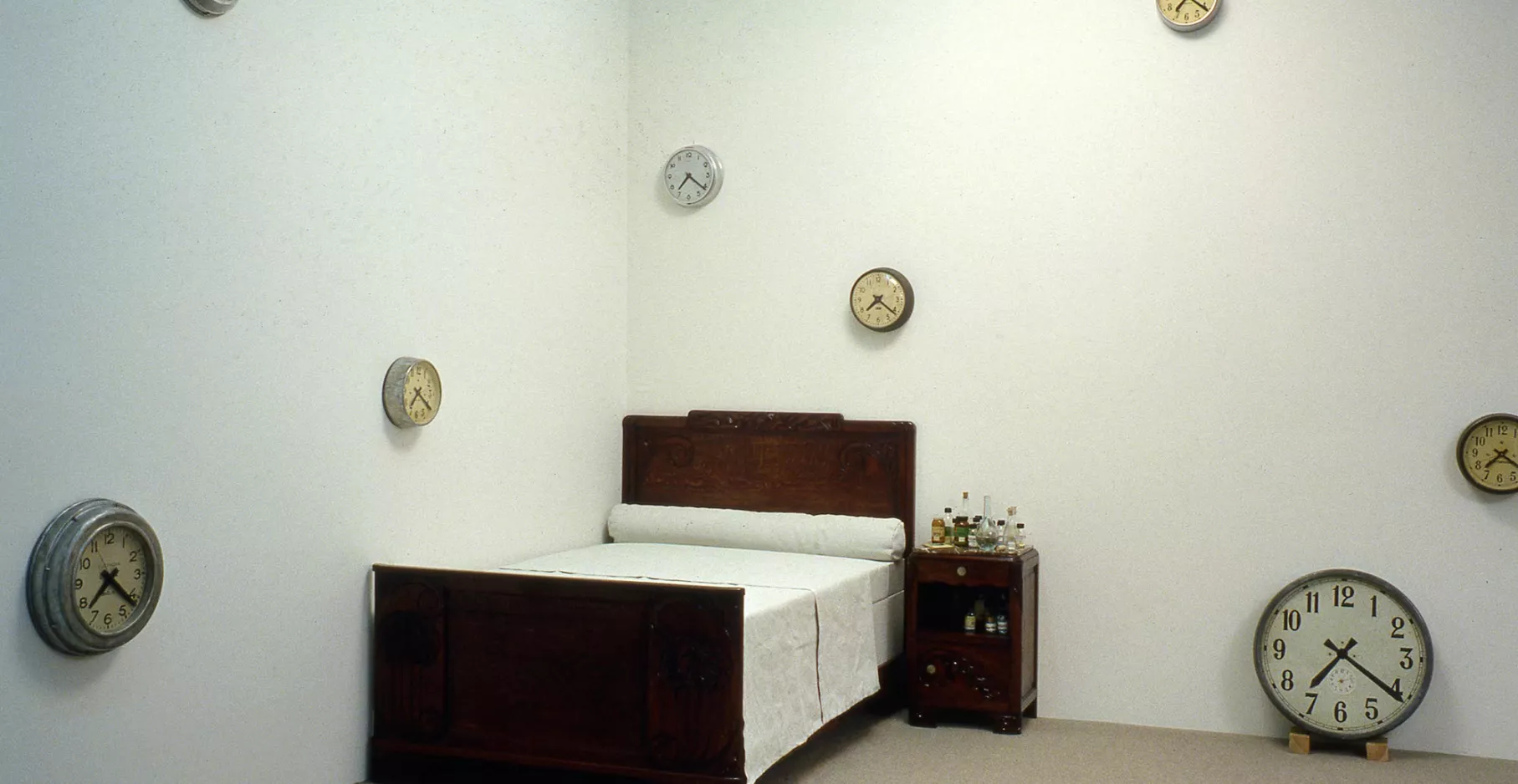 Installation d'horloges aux murs, d'un lit et d'une table de chevet au sol.