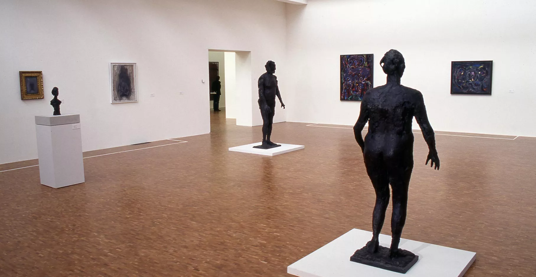 Salle d'exposition, sculptures aux centres et tableaux aux murs.