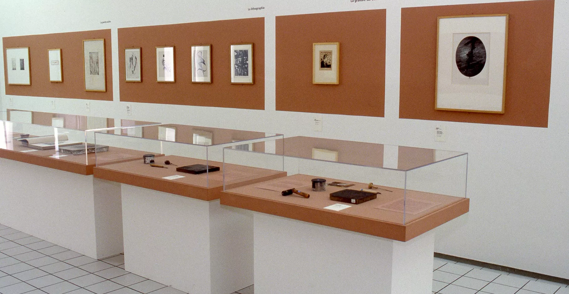 Salle d'exposition avec vitrines et œuvres au mur.