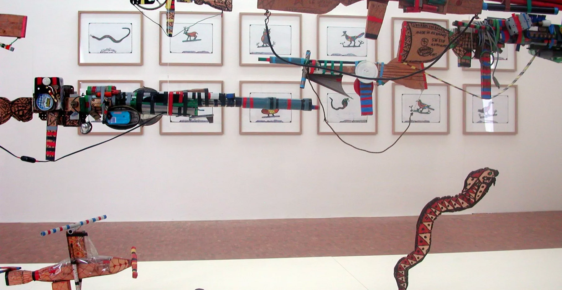 Œuvres représentant des armes en plastique de Robillard suspendues devant des dessins.