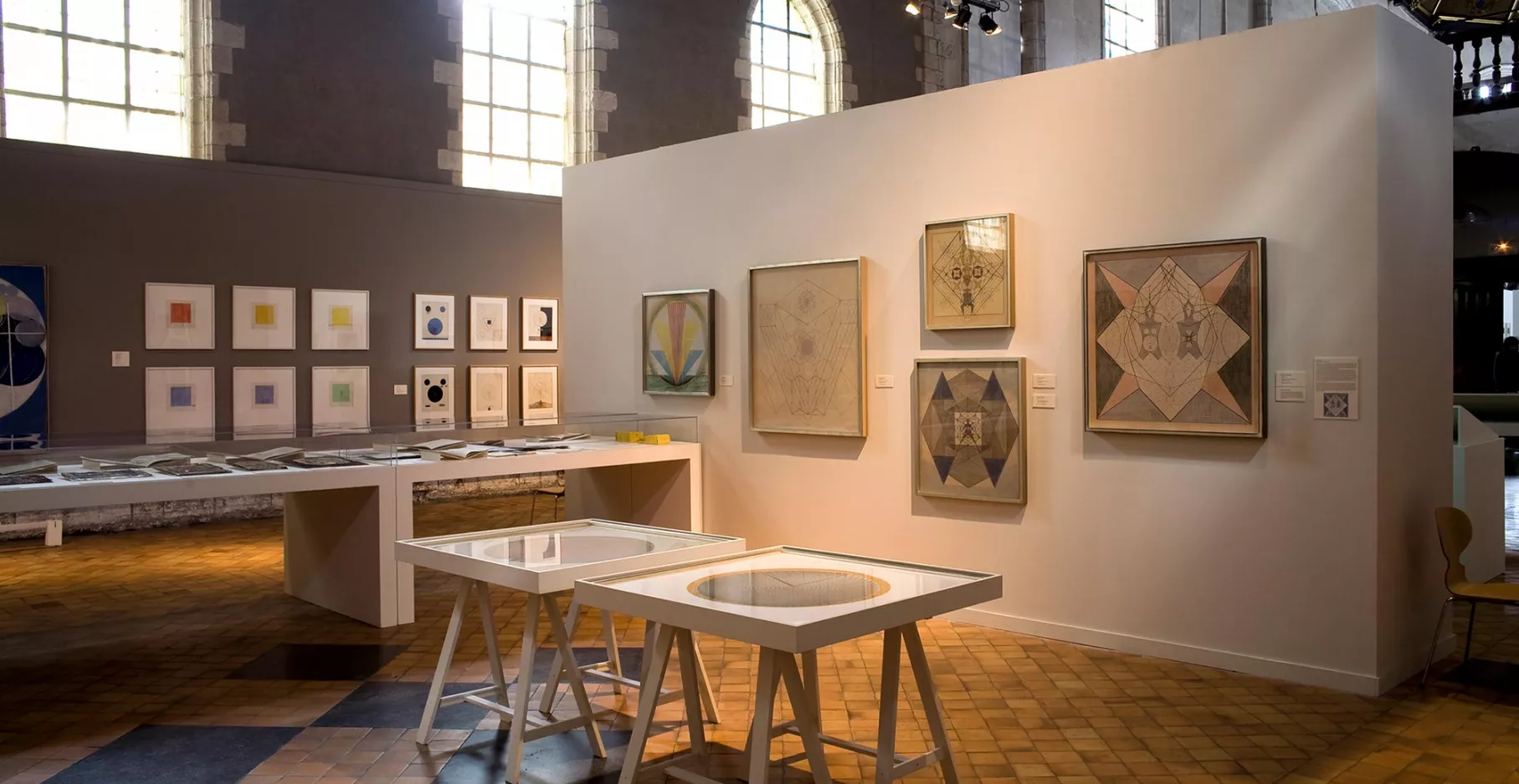 Salle d'exposition avec cimaises, tables et œuvres.