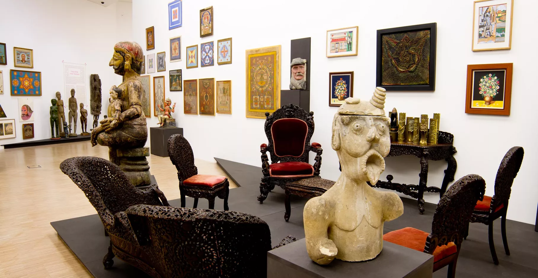 Salle d'exposition avec mobilier, sculptures et toiles au mur.