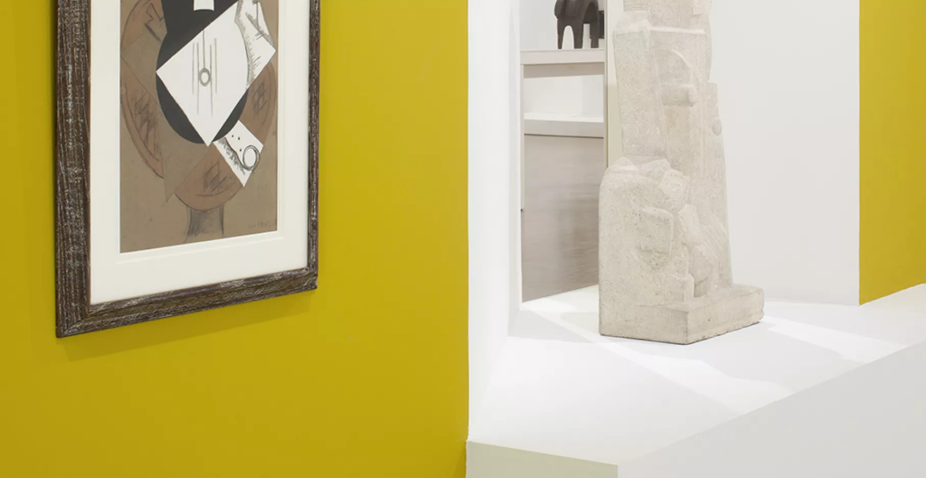 Salle d'exposition jaune et blanche avec toiles et sculptures.