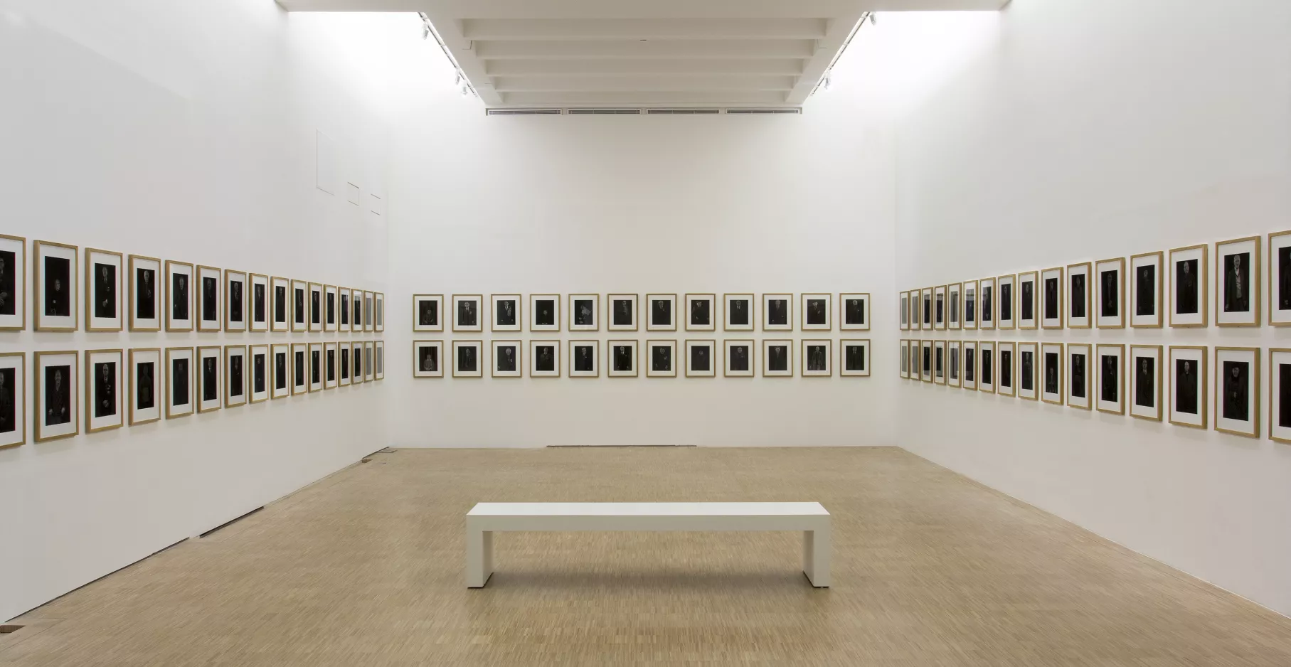 Salle d'exposition avec deux rangés de cadres et un banc.