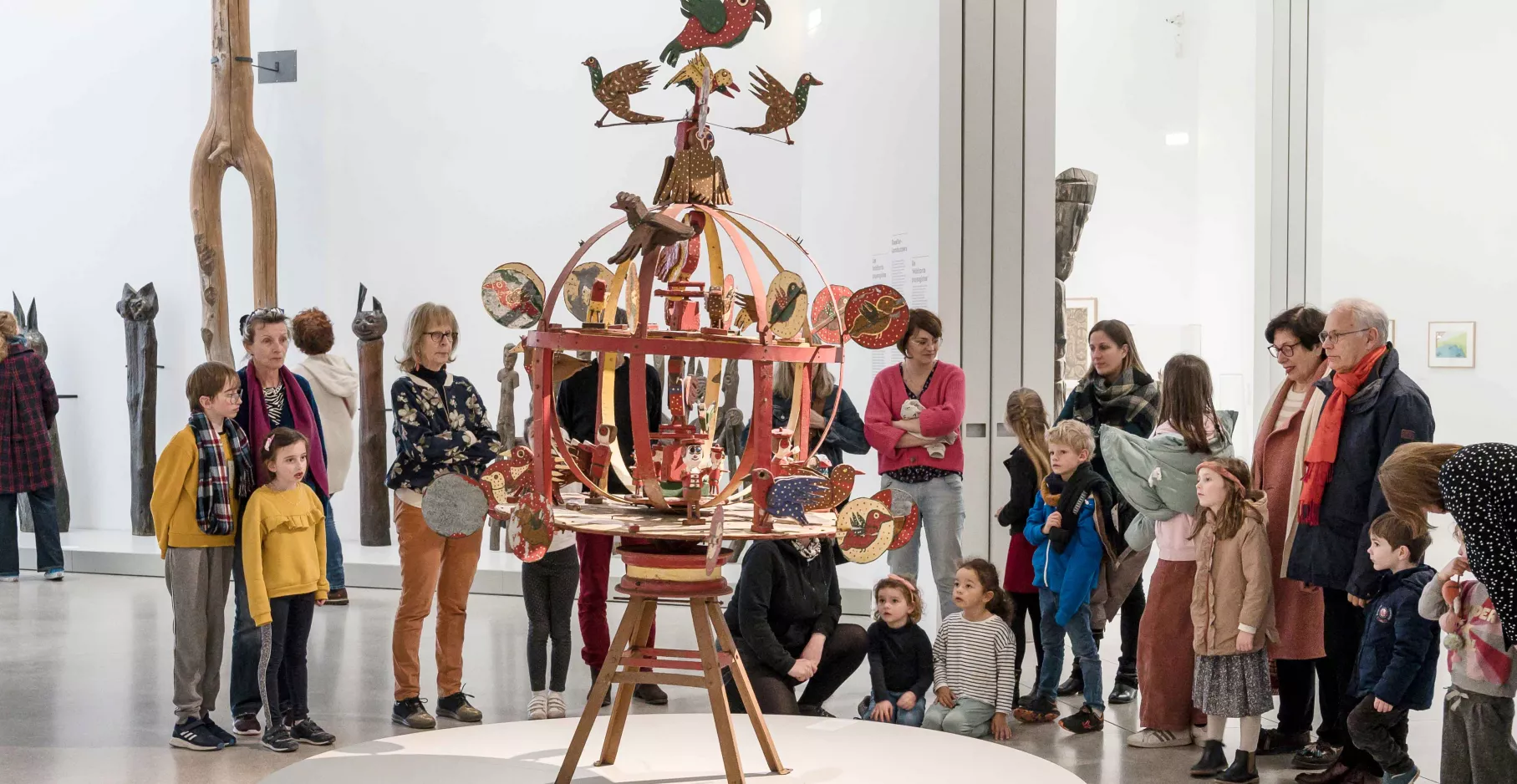 Groupe de personnes autour d'une sculpture d'art brut représentant un manège aux oiseaux.