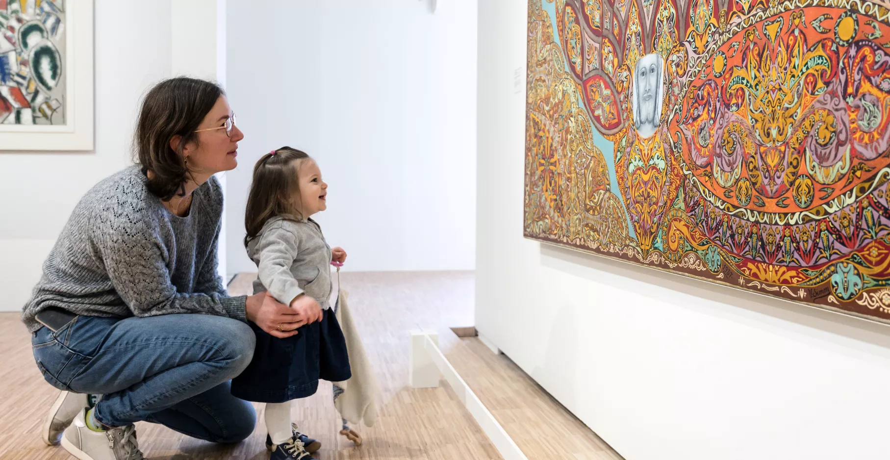 Une mère accroupi et sa toute petite fille devant une toile.