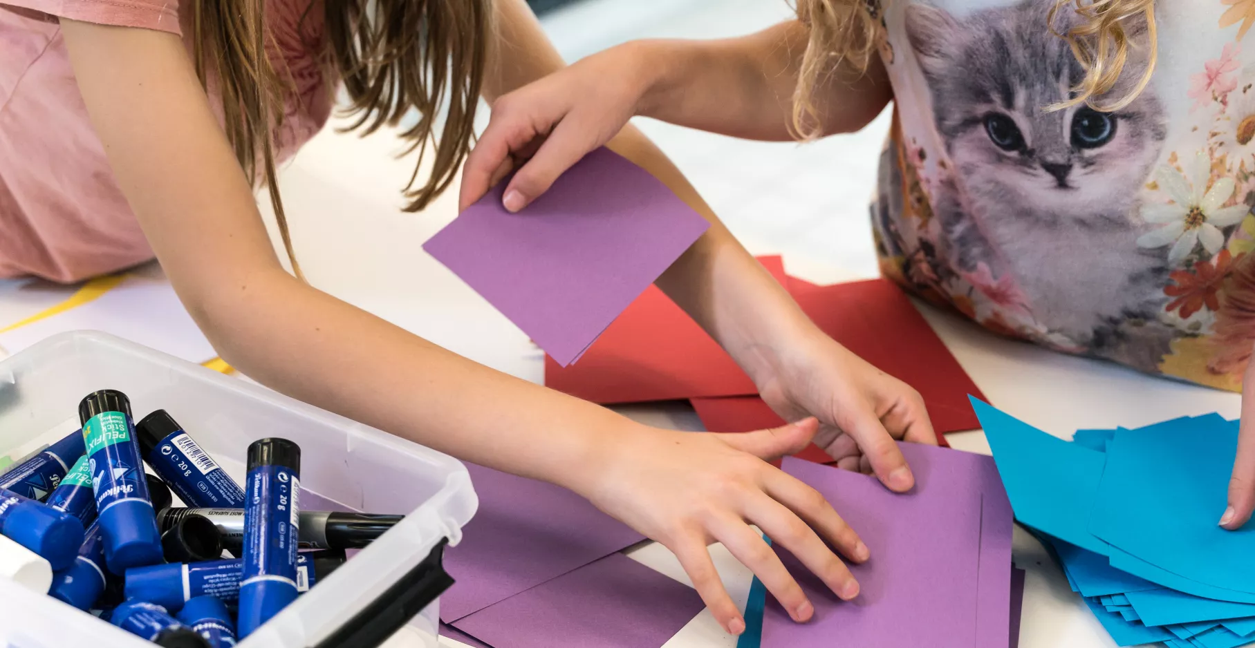 Mains en train de plier du papier coloré, à l'occasion d'un atelier.