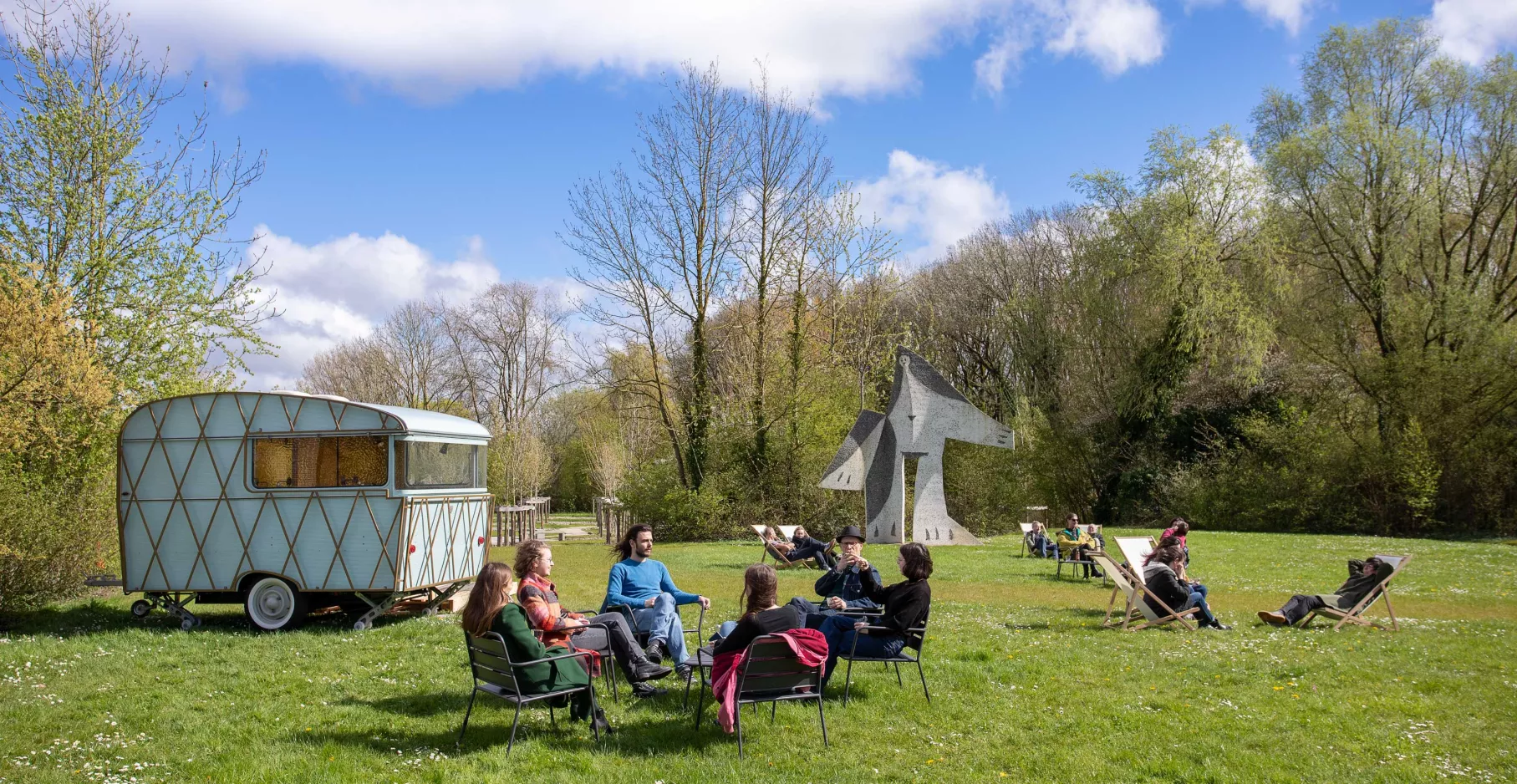 Photographie de la caravane de La Guinguette, dans le parc du musée avec un groupe de personnes.