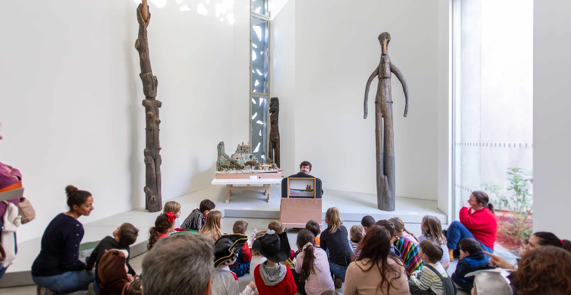 Groupe d'enfants au sol devant un guide qui montre une œuvre, à l'occasion d'un atelier vacances d'été.